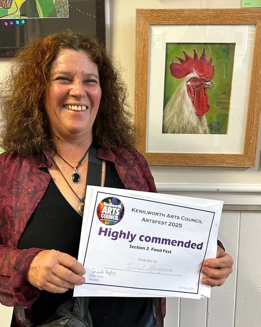 Juliet Musgrave smiling, holding her Highly Commended certificate at Kenilworth ArtsFest 2025 beside her painting 'Big Red'